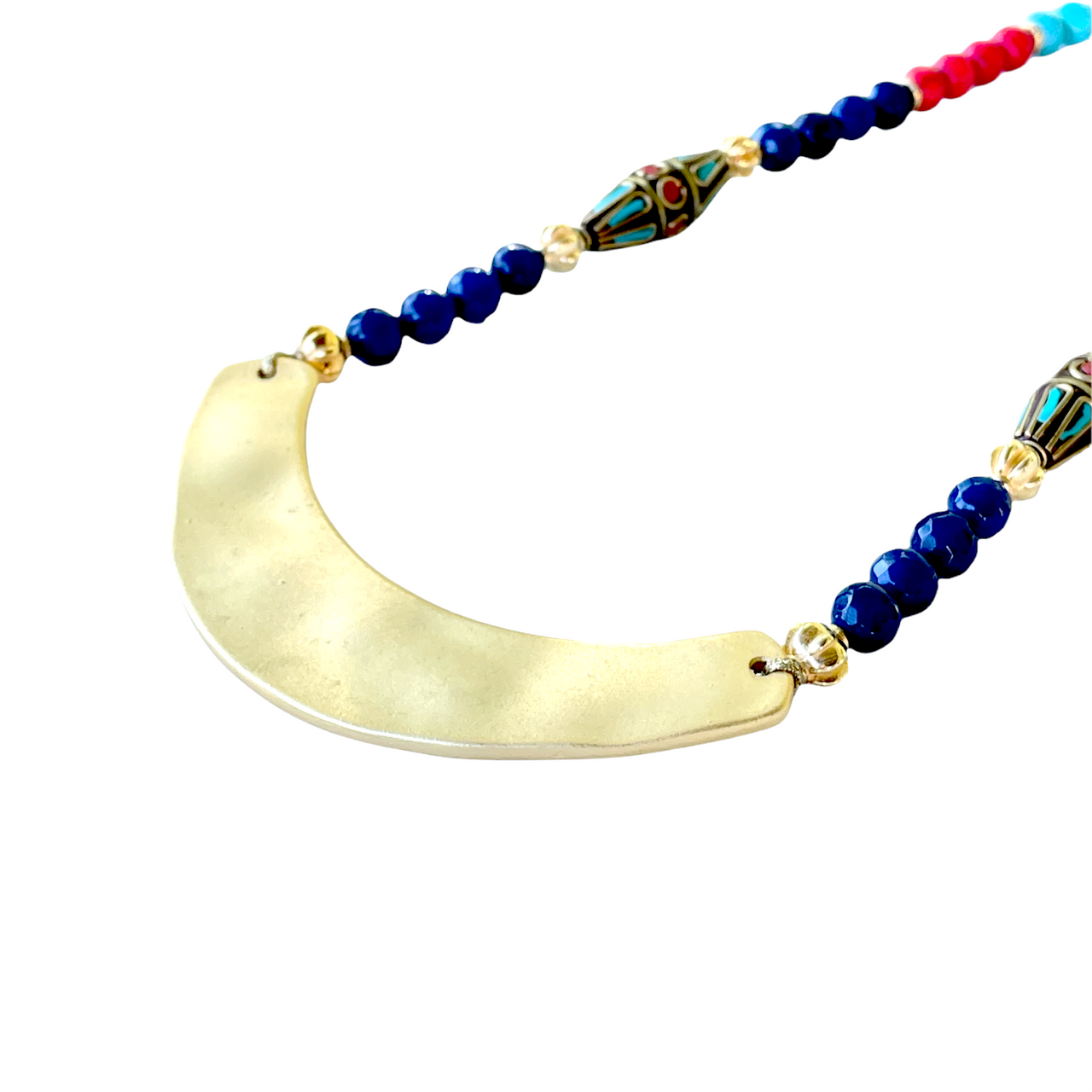 Collar de inspiración egipcio con cuentas de ágatas azul marino, cuentas de Howlite turquesa y rojas, cuentas de zamak de oro y dos piezas de zamak lacadas. Además tiene como pieza central una media luna de Zamak con baño de oro mate, que hacen de este collar una pieza espectacular. Combinalo con tu look look favorito!  Detalle